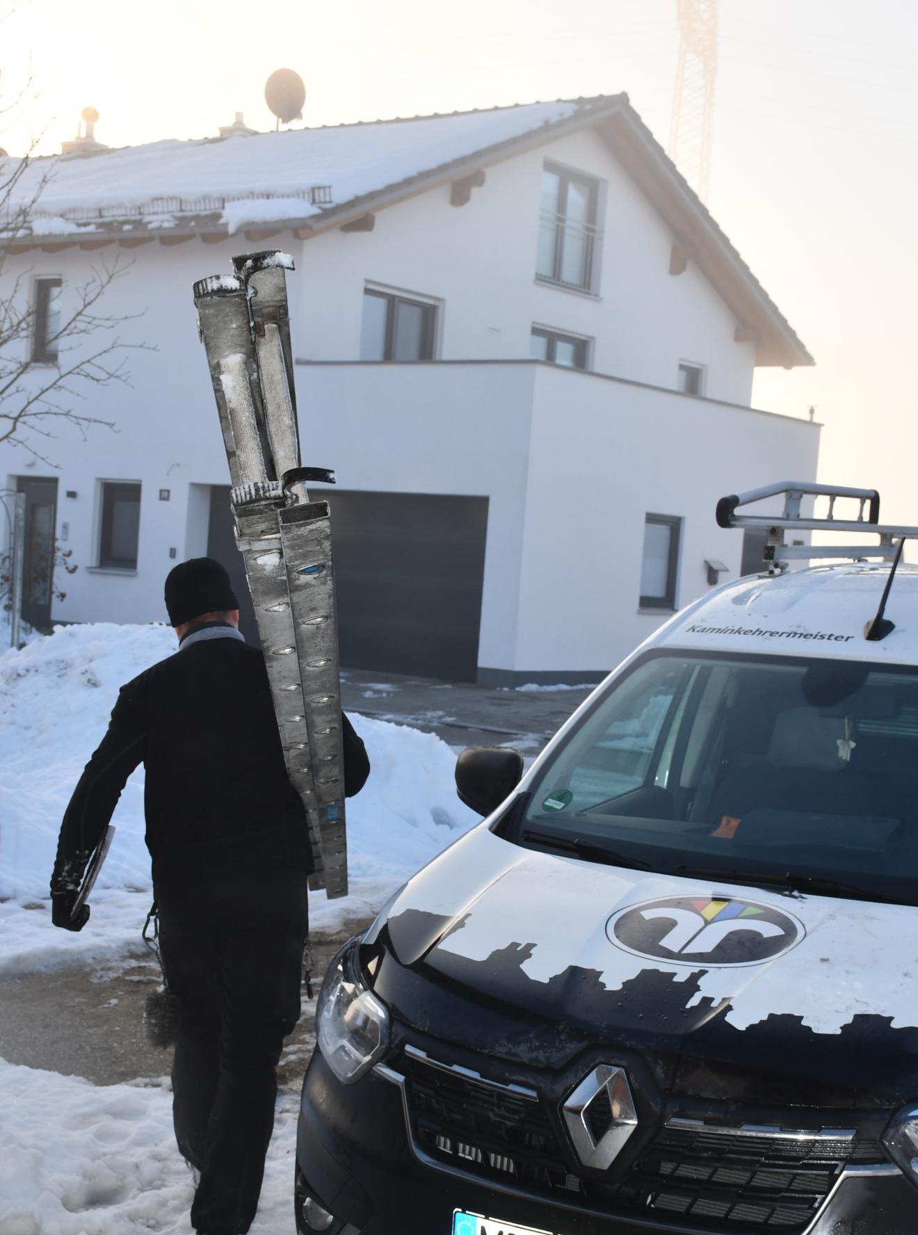 Schornsteinfeger läuft mit Leiter neben Auto auf Haus zu