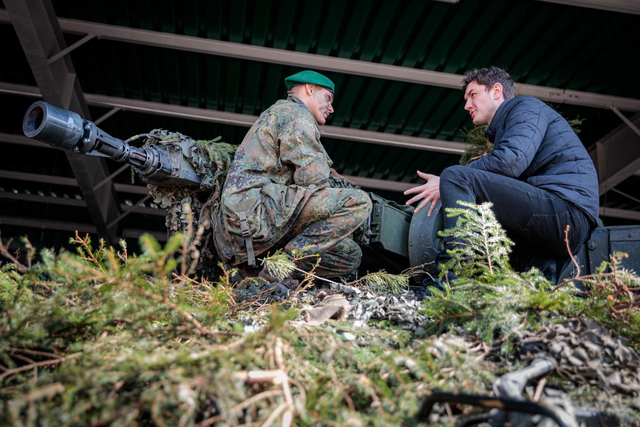 Politiker mit Soldat in Gespräch in der Hocke vor Panzer