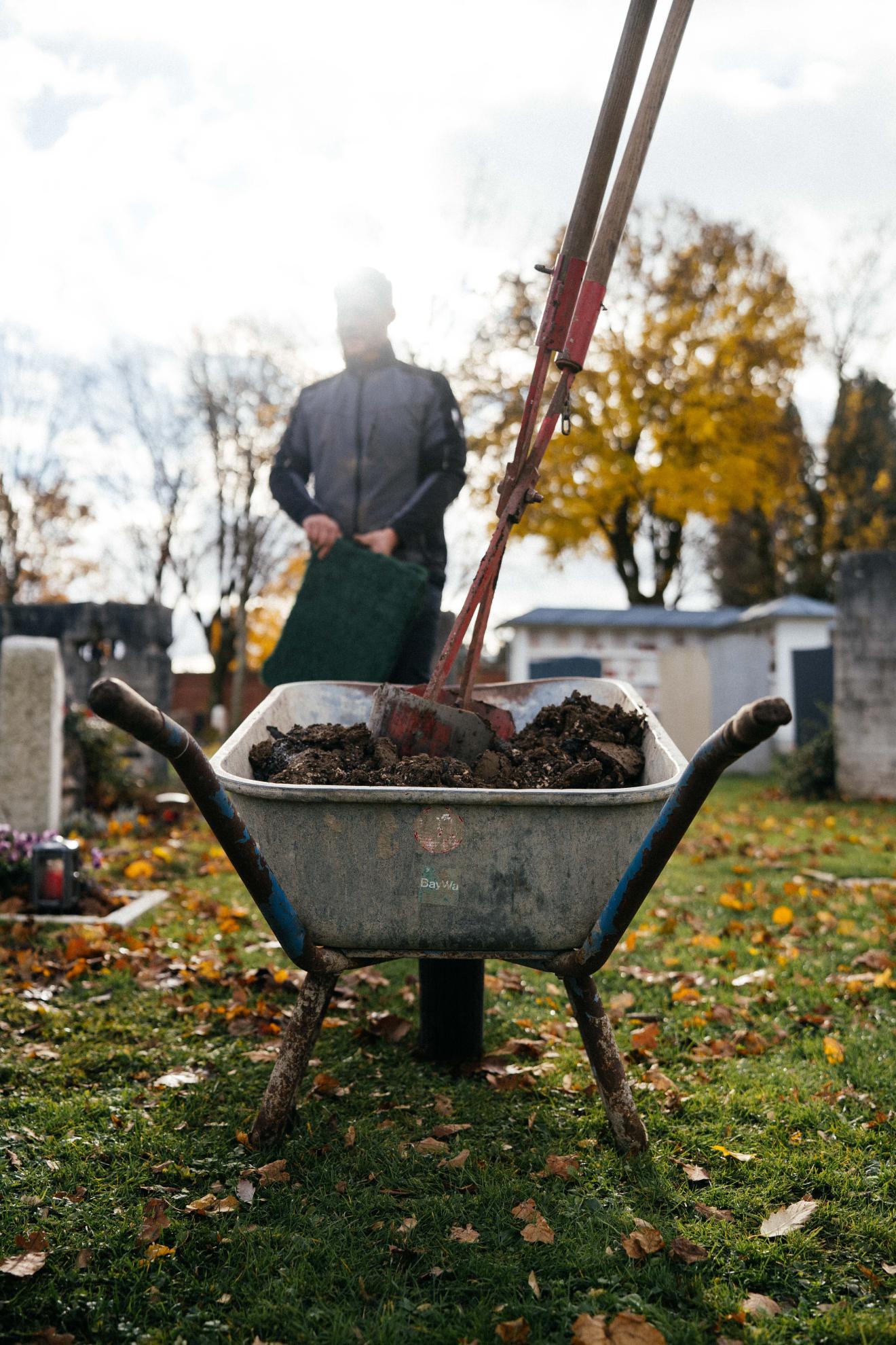 Mann steht vor Schubkarre auf Friedhof
