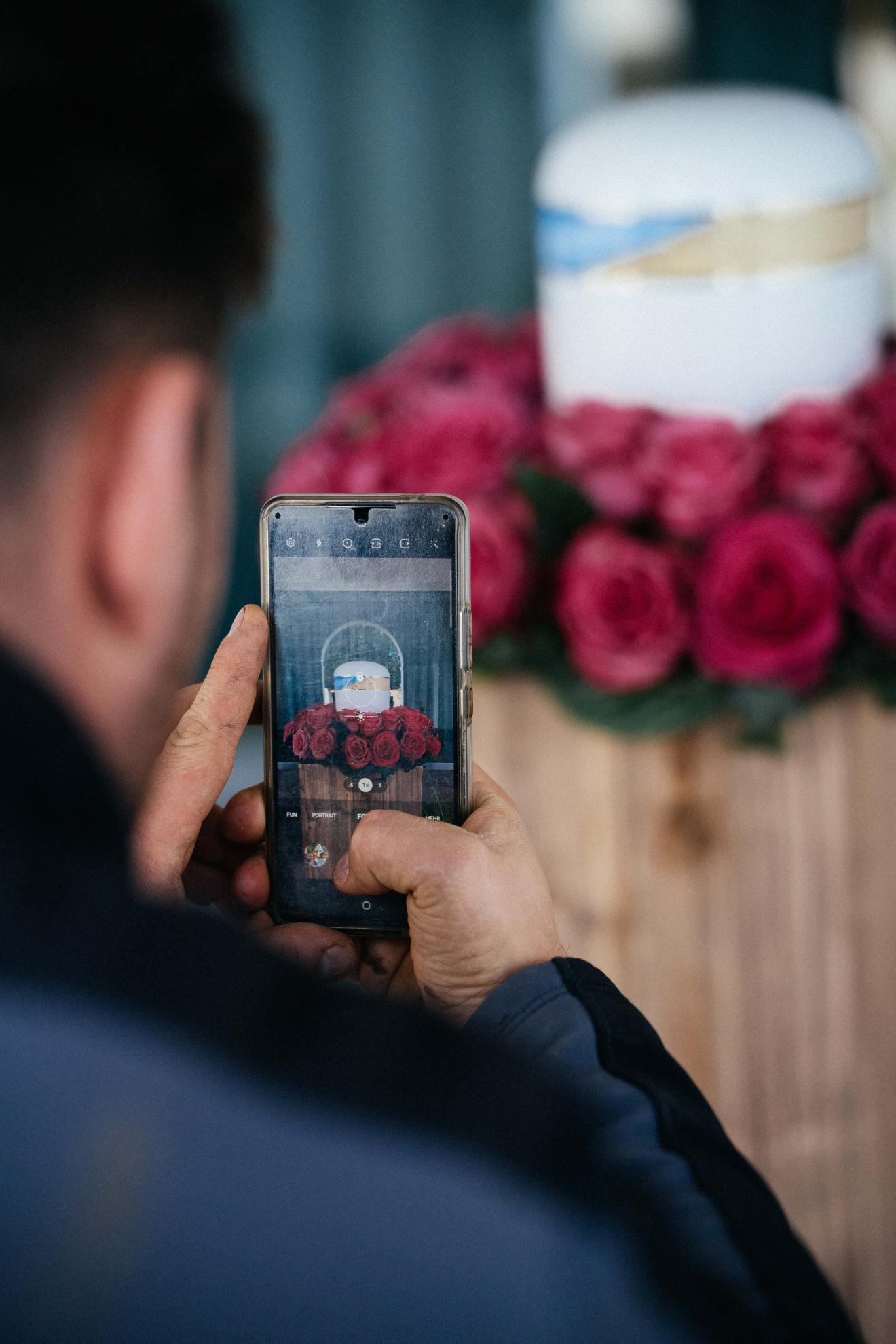 Mann fotografiert hergerichtetes Grab mit Handy