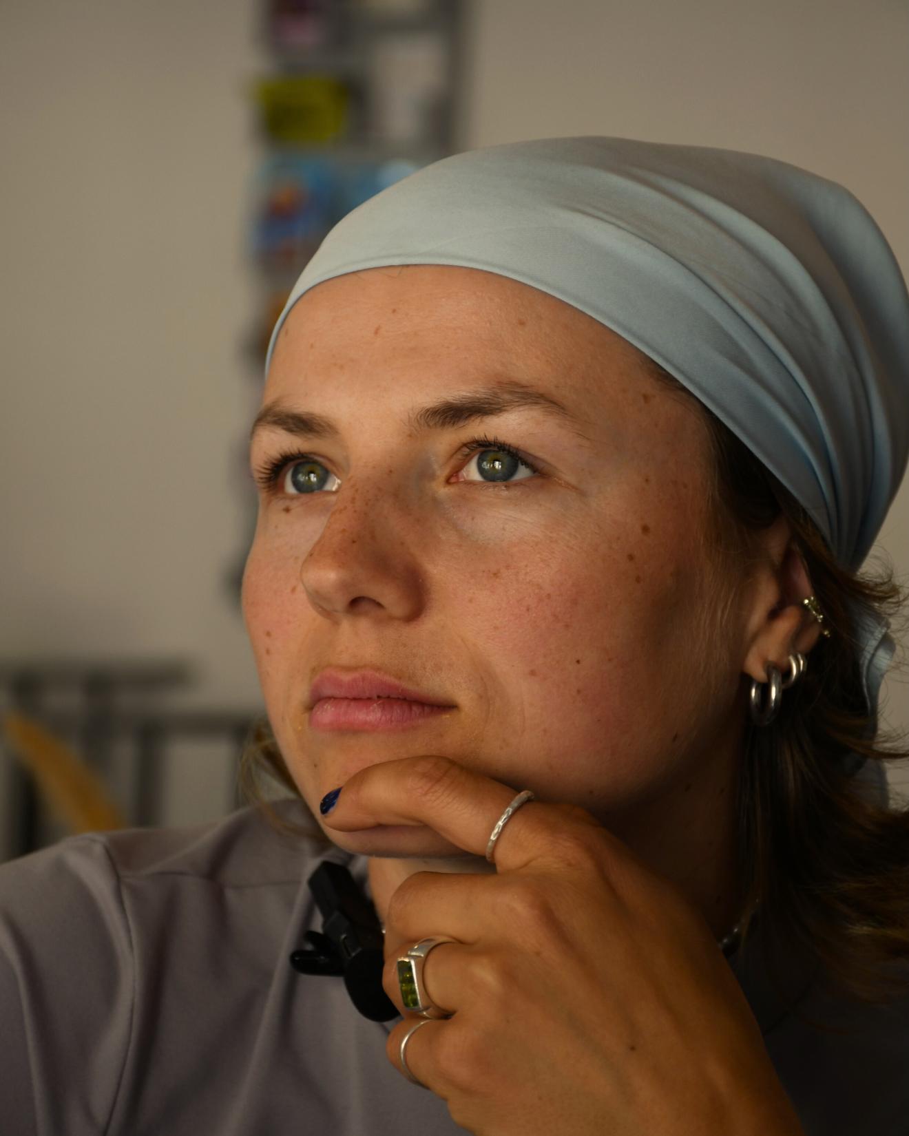 Eine junge Frau, die mit ihrer linken Hand am Kinn nachdenklich in die Ferne guckt.