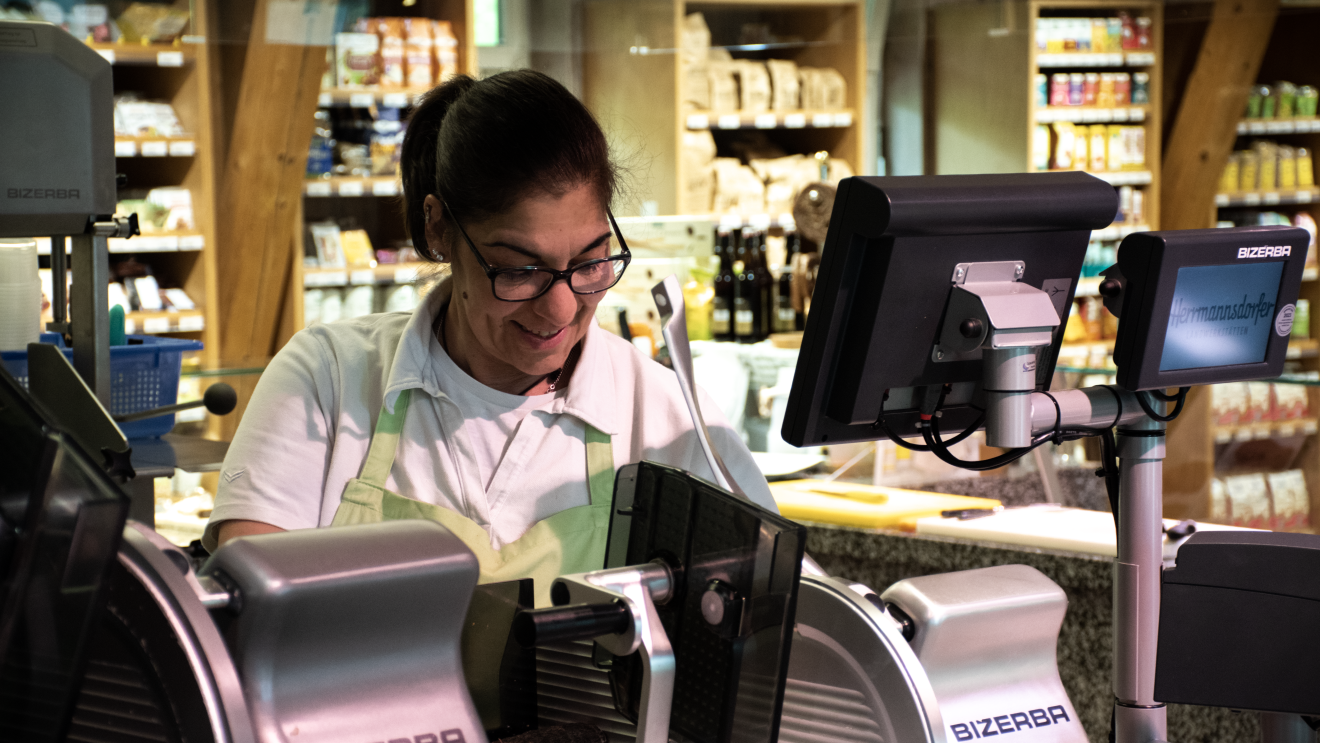 Mitarbeiterin hinter Frischetheke des Hofladens betreut Kunden