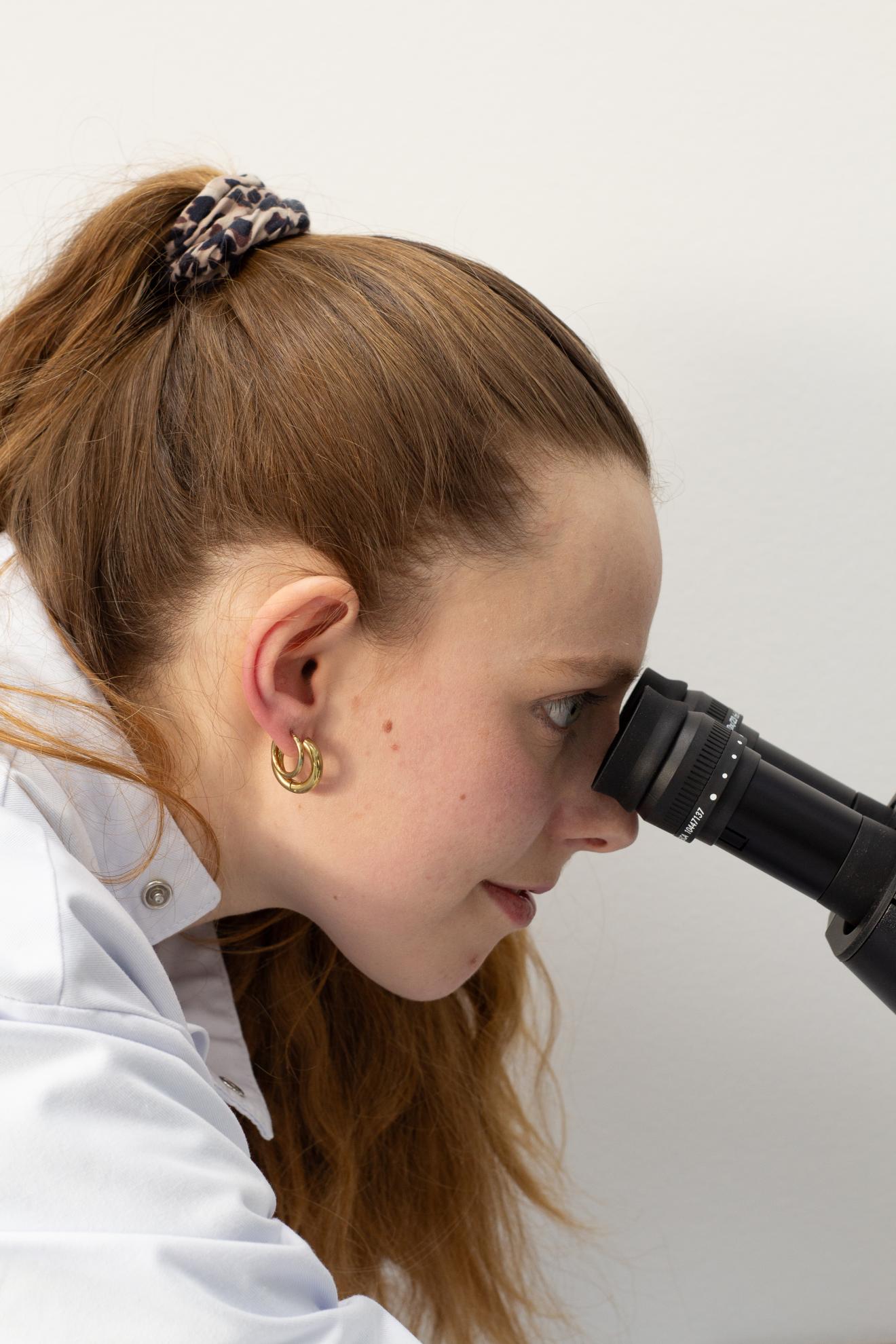 Eine Frau im Laborkittel schaut durch ein Mikroskop. 