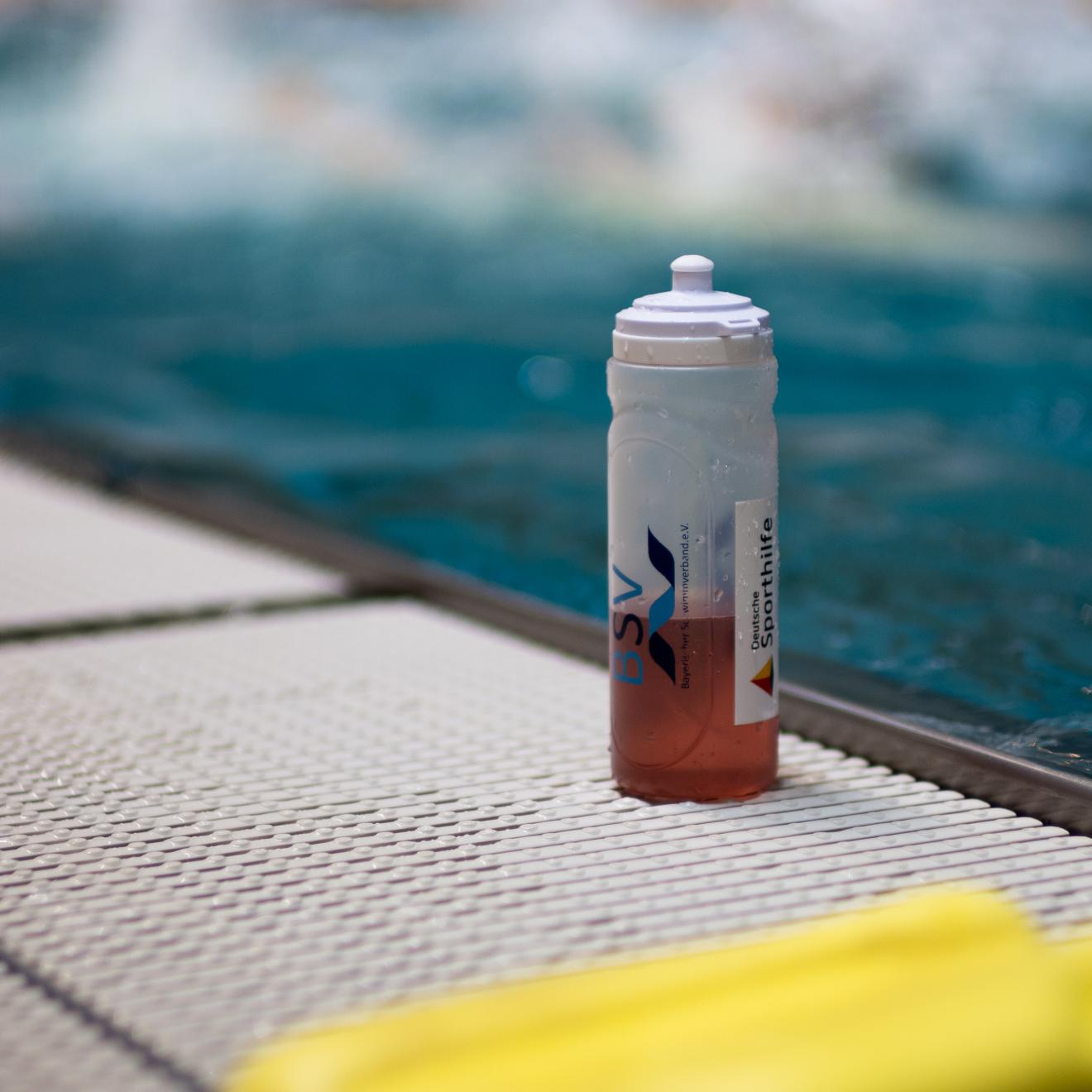 Eine Trinkflasche steht am Beckenrand des Schwimmbads.