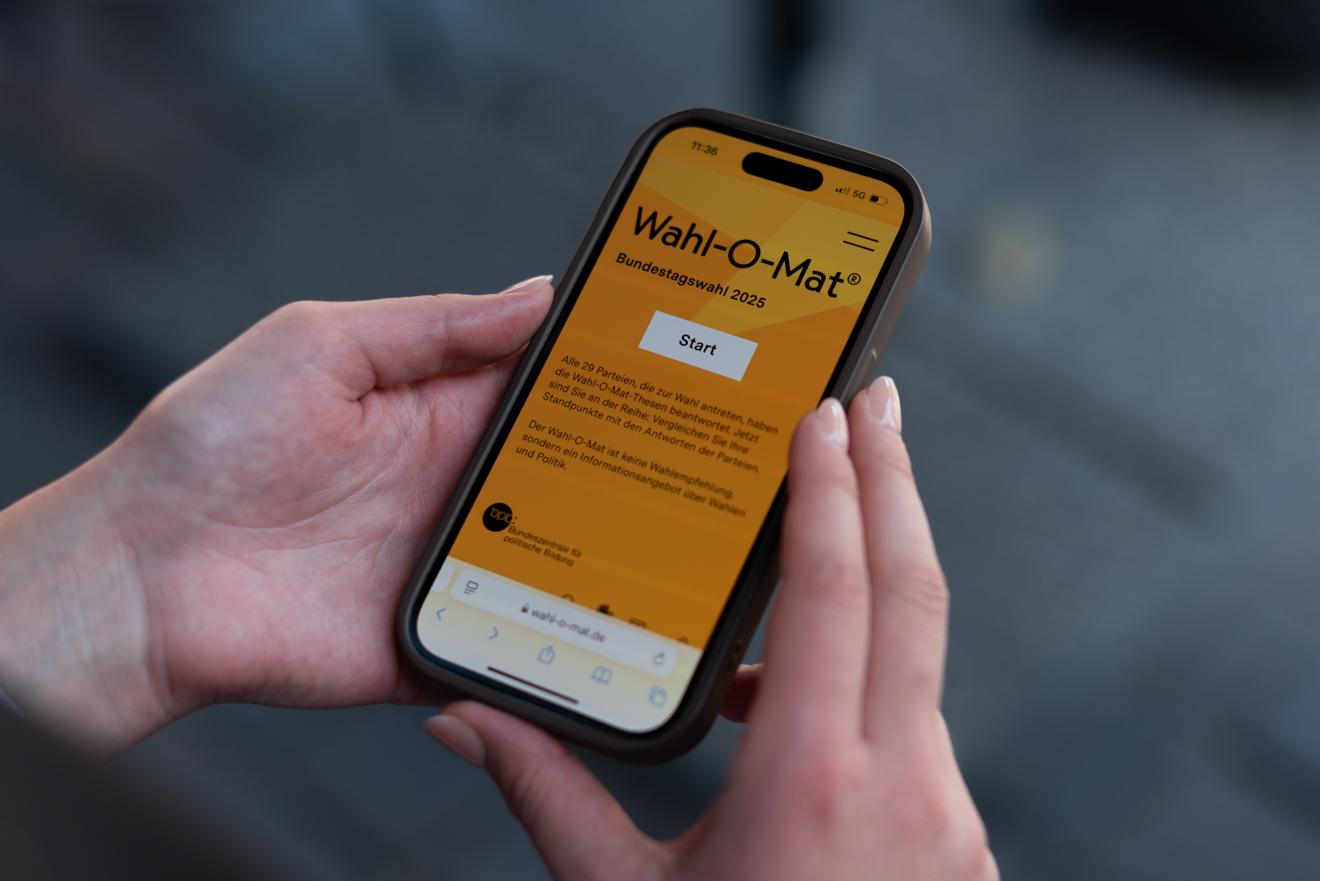 Zu sehen ist ein Handy in der Hand einer Userin mit der Wahl-O-Mat-Startseite.