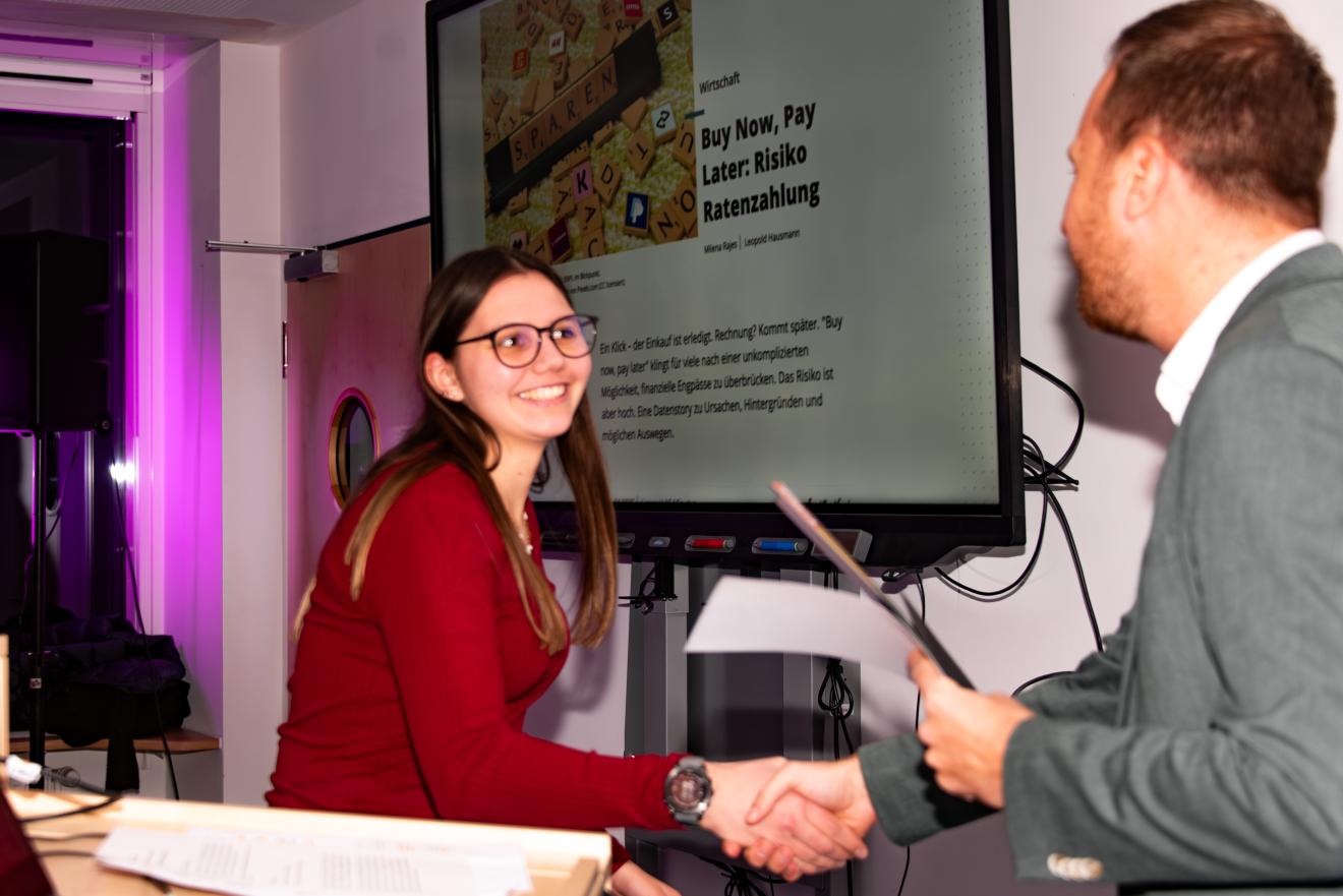 Die Übergabe erfolgt durch Prof. Schützeneder, der die Urkunde übergibt. 