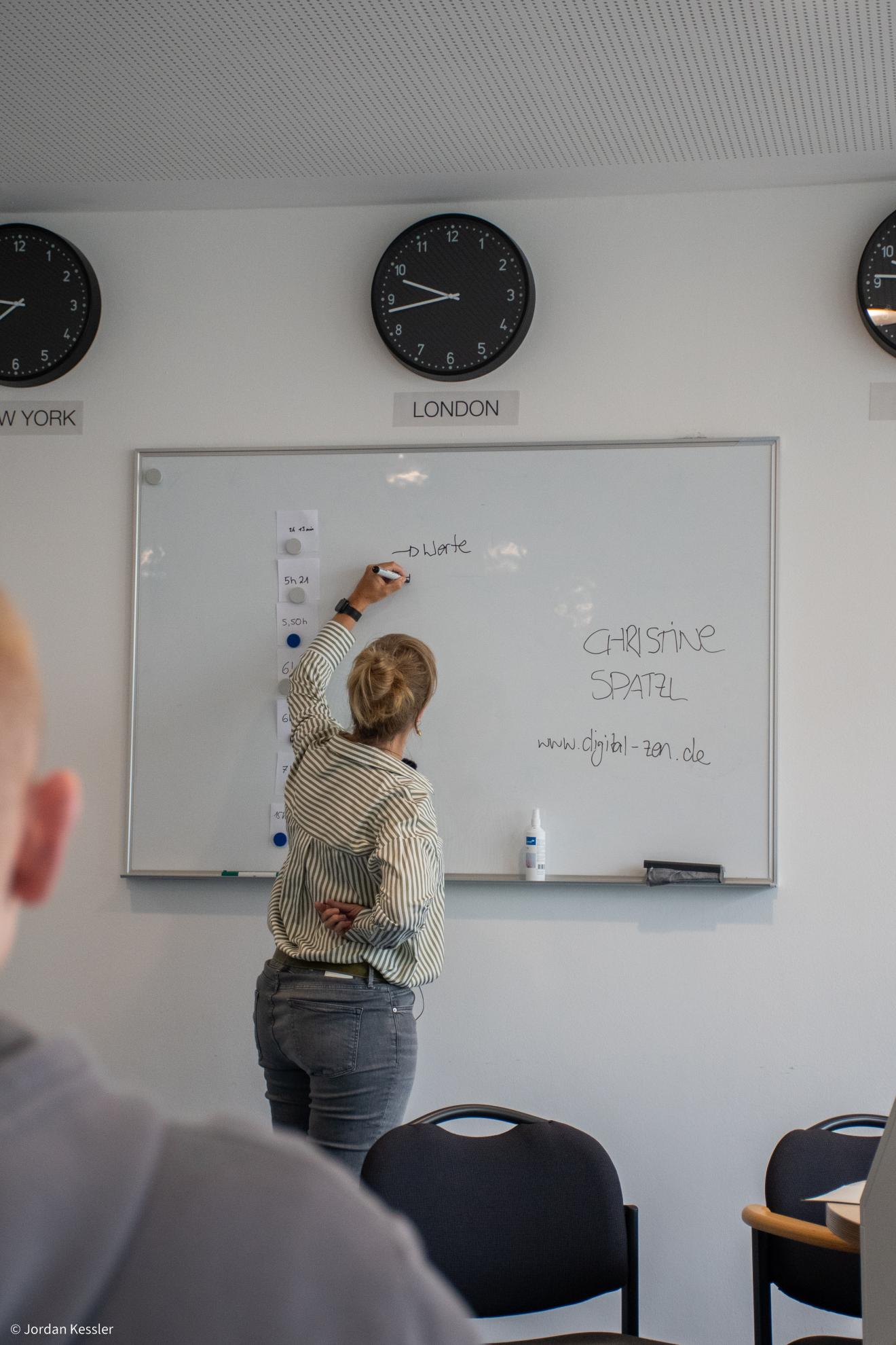 Christine Spatzl schreibt während eines Workshops an eine Whiteboard-Tafel. Auf dem Whiteboard stehen ihr Name und die Website ‚www.digital-zen.de‘.