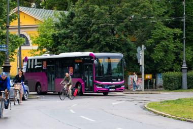 Zu sehen ist ein Bus in einem Kreisverkehr, gemeinsam mit Radfahrern.