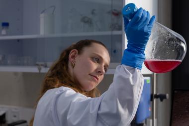 Eine Biotechnologin hält einen Mini-Bioreaktor in die Luft.