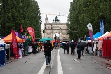 Trotz Regens informieren sich Besucherinnen und Besucher an den bunten Ständen verschiedener Parteien und Organisationen entlang der Leopoldstraße in München.
