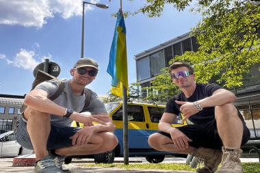 Auf dem Bild zu sehen sind Erik und Julian, welche vor einem Bus in den Nationalfarben der Ukraine knien.