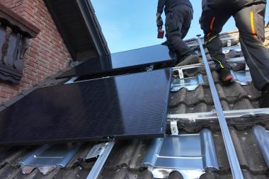 Solarpaneele auf dem Dach eines Einfamilienhauses die von zwei Handwerkern montierwerden.