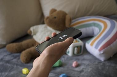 Hand mit Handy: TikTok geöffnet. Im Hintergrund ist Kinderspielzeug zu sehen.