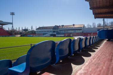 Blaue Sitzreihen vor leerem Fußballfeld
