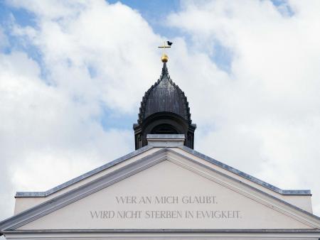 Kirchturmspitze mit Schriftzug darunter "Wer an mich glaubt, wir nicht sterben in Ewigkeit."