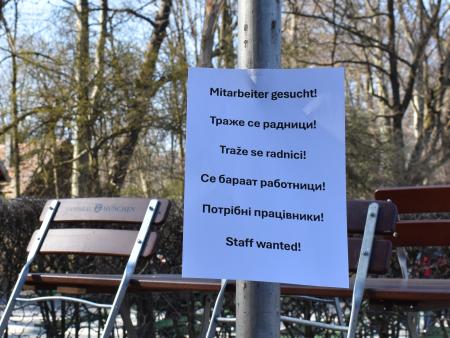 Symbolbild - leerer Biergarten und ein Schild mit "Mitarbeiter gesucht" in verschiedenen Sprachen