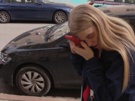 Kerstin Mirschberger steht auf einem Bürgersteig und hält sich das Handy direkt vor ihr Auge um etwas erkennen zu können.