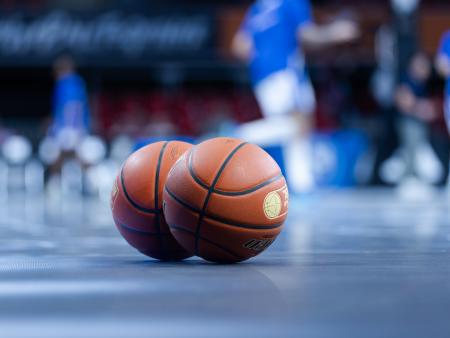 Zwei Basketbälle liegen auf dem Court. Spieler im Hintergrund.