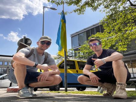 Auf dem Bild zu sehen sind Erik und Julian, welche vor einem Bus in den Nationalfarben der Ukraine knien.
