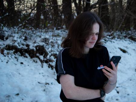 Person im T-Shirt steht im Schnee und schaut auf ihr Handy.