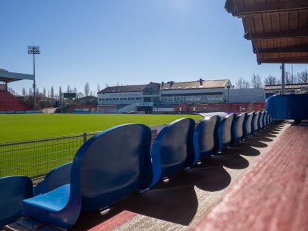Blaue Sitzreihen vor leerem Fußballfeld