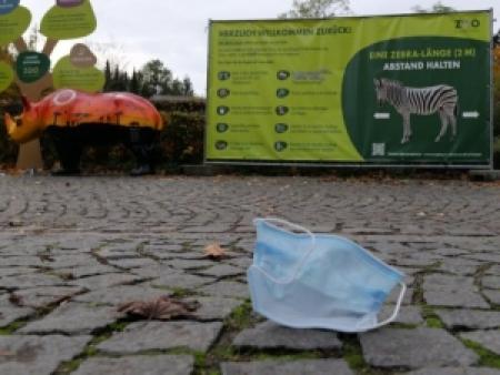 Ein chirurgische Maske liegt vor dem Plakat des Augsburger Zoos auf dem Boden.