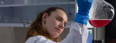 Eine Biotechnologin hält einen Mini-Bioreaktor in die Luft.